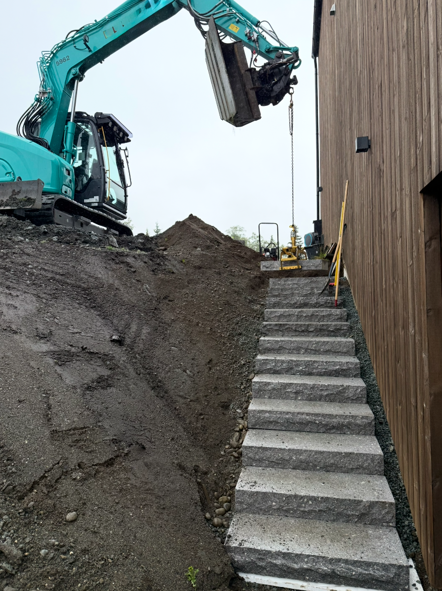 Gravemaskin under bygging av steintrapp i terreng